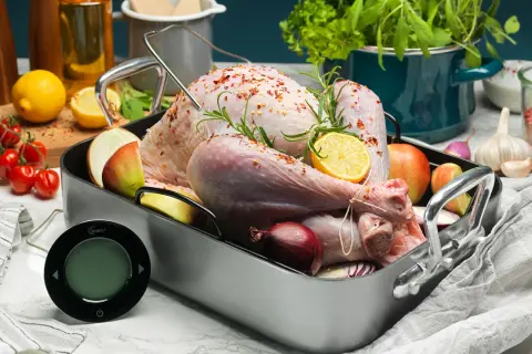 En rå kalkon i ugnsform med citron, lök och äpple. En digital termometer ligger redo för att mäta innertemp kalkon.