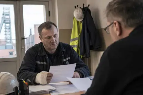 Górnik z opatrzoną ręką omawia dokumenty. Wypadek przy pracy to każde zdarzenie, które może się wydarzyć w miejscu pracy.