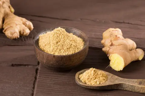 Ingwerpulver verwendung: frischer Ingwer und eine Schale mit feinem Ingwerpulver auf dunklem Holz.