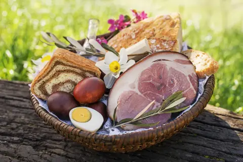 Koszyk z tradycyjnym post paschalny: chleb, jajka, wędzonka i kwiaty.