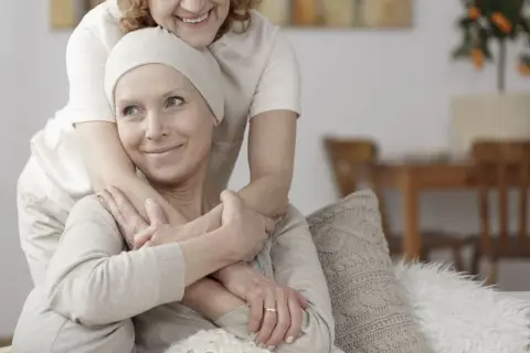Dwie kobiety przytulają się. Jedna z nich, w chustce na głowie, uśmiecha się. To obraz wsparcia w trudnych chwilach, gdzie leczenie paliatywne oferuje komfort i godność.