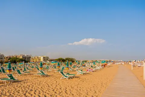 Szeroka, piaszczysta plaża w Bibione z rzędami leżaków i parasoli pod błękitnym niebem.