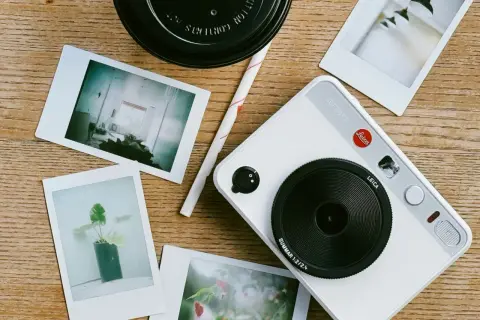 A white Leica Sofort 2 camera with instant photos scattered around. This setup inspires ideas on how to organize photos into folders.