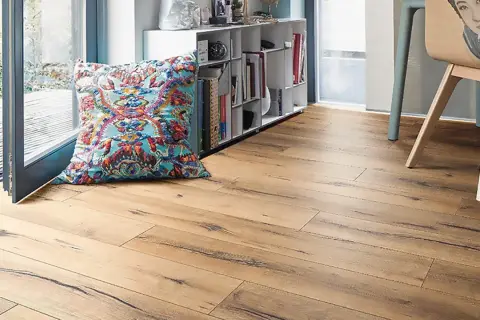 Un suelo laminado de madera clara con un cojín colorido y una estantería llena de libros.