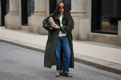 Stylische Frau in dunkelgrünem Mantel und Barrel Jeans, die sie lässig kombiniert. Sie trägt eine weiße Rollkragenpullover und auffällige Schuhe.