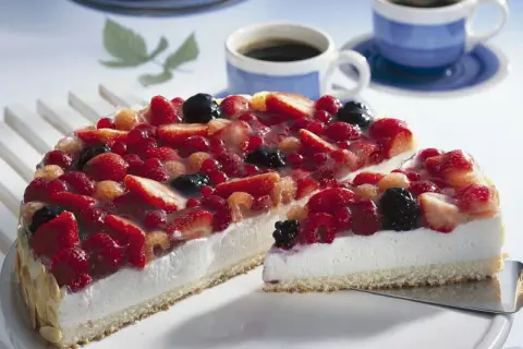 Eine einfache Torte mit frischen Beeren, bedeckt mit Tortenguss. Daneben zwei Tassen Kaffee.