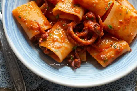 Paccheri con sugo di calamari, un piatto di mare saporito e colorato, con tentacoli che spuntano dalla pasta.