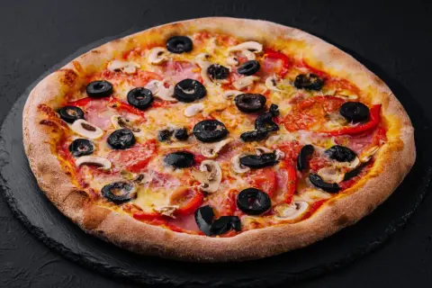 Chrupiąca pizza z oliwkami, pieczarkami i papryką na czarnym tle.