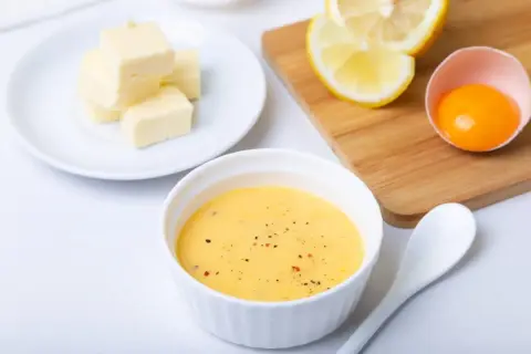 Tazón con salsa holandesa, mantequilla en cubos, limón y yema de huevo. Ingredientes para una deliciosa salsa.