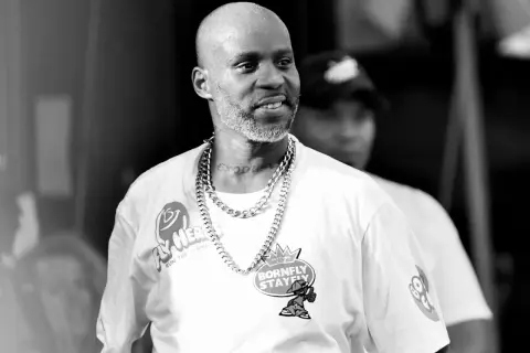 DMX w białej koszulce z łańcuchem na szyi, z tatuażem "EXODUS" na karku, uśmiecha się podczas występu.