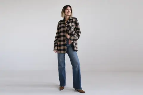 Kobieta w beżowo-czarnej koszuli w kratę i jeansach, prezentująca styl country.