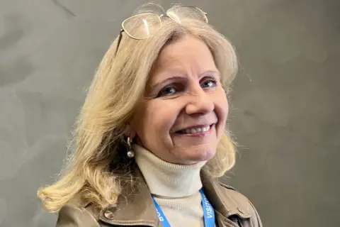 Helene Barnekow ler mot kameran, med glasögon på huvudet och en beige polotröja under en brun jacka.