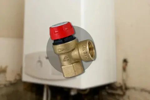 Gros plan sur un montage soupape de sécurité chaudière en laiton avec un capuchon rouge, installé sur une chaudière blanche.
