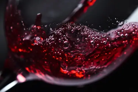Czerwone wino bez cukru, z bąbelkami unoszącymi się na powierzchni, nalewane do kieliszka.