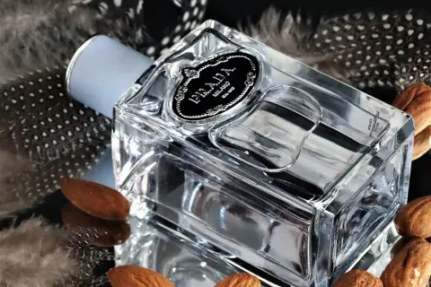 Elegancka butelka Prada Infusion d'Amande otoczona piórami i migdałami, tworząc subtelną kompozycję.