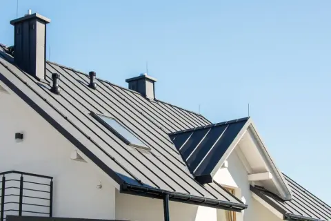 Nowoczesny dom z czarnym, metalowym dachem i kominami. Dachówka przypomina łuski świetlików, odbijając światło.