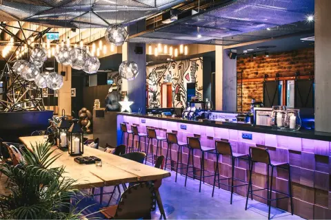 Nowoczesny bar w Moxy Hotels Pyrzowice z neonowym oświetleniem, drewnianym blatem i artystycznymi muralami.