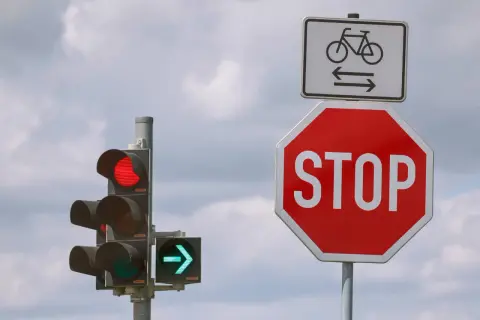 Ampel zeigt Rot, daneben ein Stoppschild. Wie lange halten? Radweg-Schild darüber.