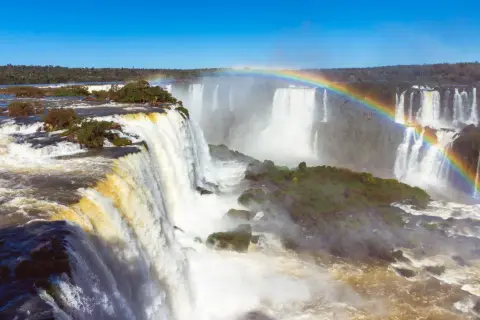 Potężny wodospad Iguazu, z tęczą unoszącą się nad mgłą wodną, otoczony bujną zielenią.