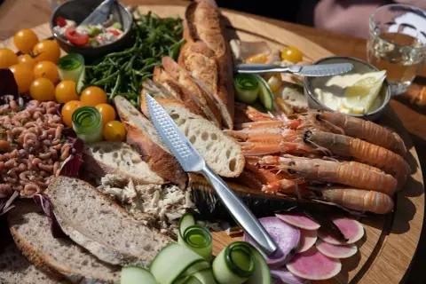 Ein Festmahl mit fisch tapas: Garnelen, Brot, geräucherter Fisch, Tomaten und Gurken auf einem Holzteller.