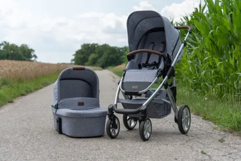 Grauer Kinderwagen mit passender Babywanne, Modell abc Salsa 4, steht auf einem Feldweg neben Maisfeld.