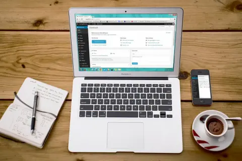 Laptop z panelem WordPress, obok notatnik z planami i telefon. Idealne narzędzia do pracy z XAMPP i WordPress.
