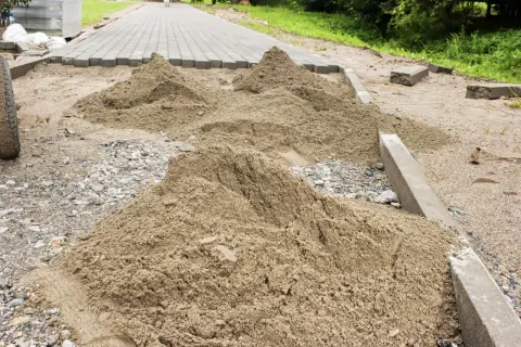 Kopa piasku czeka na ułożenie kostki brukowej. Trudno oszacować, ile piasku na m2 kostki, ale widać, że materiału jest sporo.