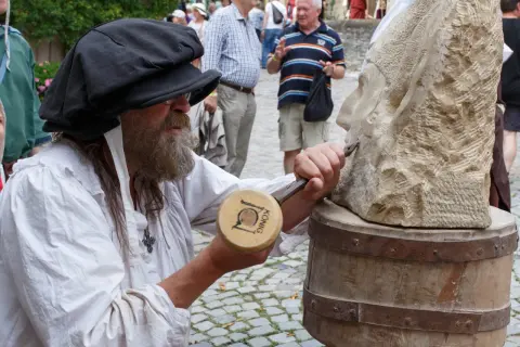 Steinmetz bei der Arbeit am Bad Wimpfen Zunftmarkt. Ein Mann mit Bart und schwarzer Kappe meißelt an einer Steinskulptur.