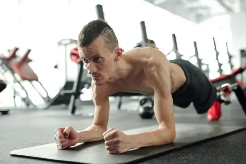 Un homme concentré effectue un gainage dynamique sur un tapis de gym, muscles tendus, dans une salle de sport.