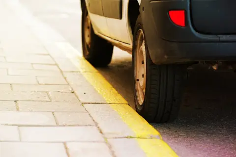 Un coche aparcado junto a una acera con marcas viales amarillas. El significado de estas marcas viales amarillas indica prohibición de estacionar.