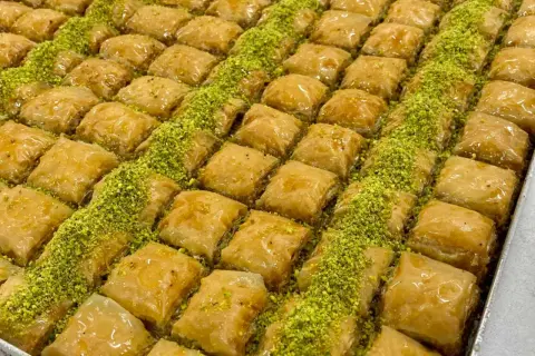 En stor bricka med gyllene, krispiga baklavabitar, generöst strödda med gröna pistagenötter. Perfekt för ett hemlagat baklava recept.