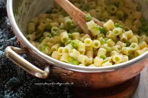 Un primo piatto cremoso di pasta e piselli, mescolata con un cucchiaio di legno in una pentola di rame.