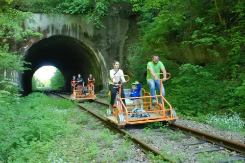 Rodzina na drezynach w Bieszczadach, przejeżdża obok tunelu w otoczeniu zieleni.