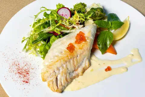 Filet de haddock parfaitement cuit, garni de perles de hareng, servi avec une salade fraîche, des légumes et une sauce crémeuse.