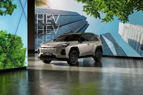 Nowoczesny srebrny Toyota RAV4 HEV prezentowany na tle futurystycznych budynków i zieleni.