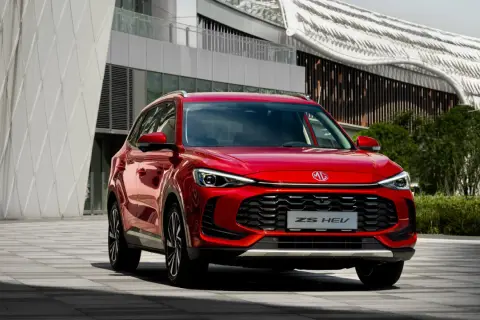Czerwony MG ZS HEV, nowoczesny SUV, zaparkowany przed futurystycznym budynkiem.