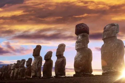 Kamienne posągi Moai na Wyspie Wielkanocnej o zachodzie słońca.