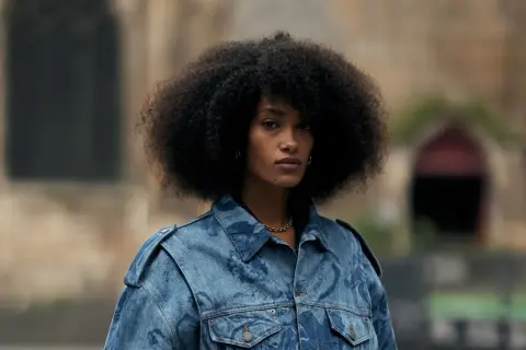 Frau mit Afro-Frisur trägt eine auffällige Jeansjacke, die perfekt zu einem lässigen Baggy Jeans Outfit passt.