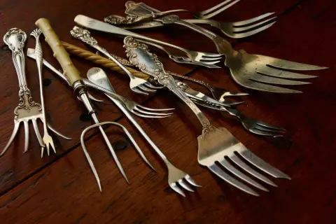 Un assortiment de fourchettes anciennes, certaines ornées, sur fond de bois. Qui a inventé la fourchette ? Ces ustensiles racontent une histoire.