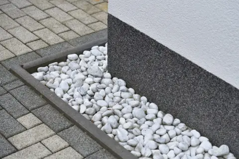 Grus runt huset med stenläggning och en mörk, strukturerad vägg.