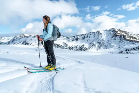 Frau mit Rucksack und Skitourenausrüstung in verschneiter Berglandschaft. Perfekte Packliste Skitour für Abenteuer.