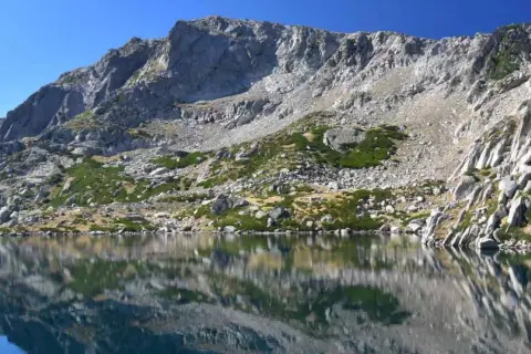Reflets parfaits des montagnes rocheuses sur le lac de Bastani, sous un ciel bleu éclatant.