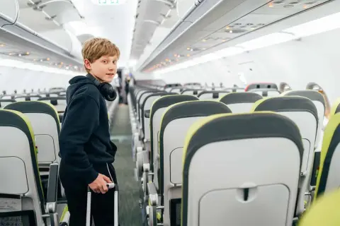 Chłopiec z walizką i słuchawkami na szyi w samolocie. Wizzair od ilu lat można latać samemu?