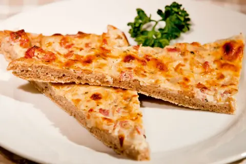 Drei Stücke herzhafter Blooz mit Speck und Zwiebeln auf einem Teller, garniert mit Petersilie. Ein köstliches Blooz-Rezept.