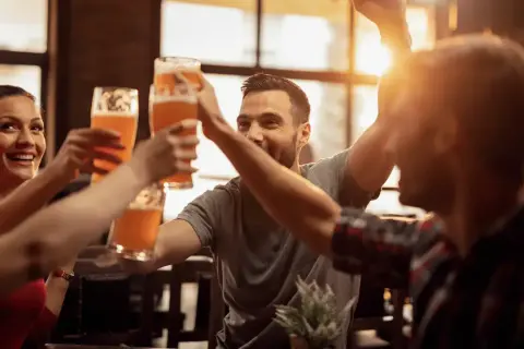 Uśmiechnięci ludzie wznoszą toasty piwem w jednym z najlepszych pubów w Warszawie.