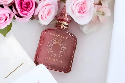 Różowe róże otaczają flakonik perfum Charlotte Tilbury Love Frequency.