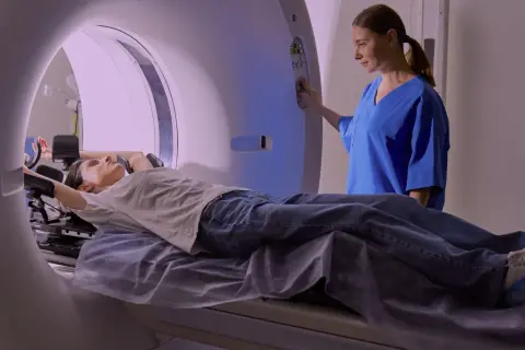 En patient ligger på en brits i en MR-scanner, medan en sjuksköterska justerar inställningarna. Mr Ryggs undersökning pågår.