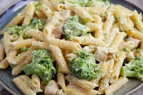 Penne z kurczakiem i kremowym sosem, w którym dominują zielone różyczki brokułów. Danie posypane startym parmezanem.