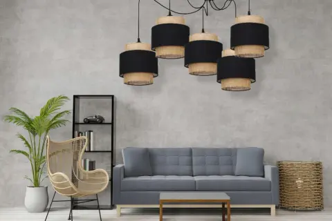 Pięcioramienna lampa pająk boho z abażurami z plecionki i czarnego materiału nad szarą sofą.