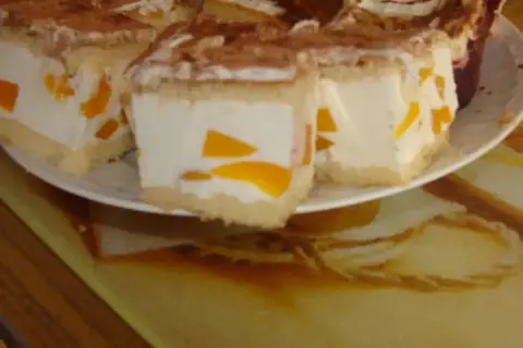 Sernik z bitą śmietaną Siostry Anastazji, z kawałkami brzoskwiń, posypany kakao. Pyszny deser na talerzu.